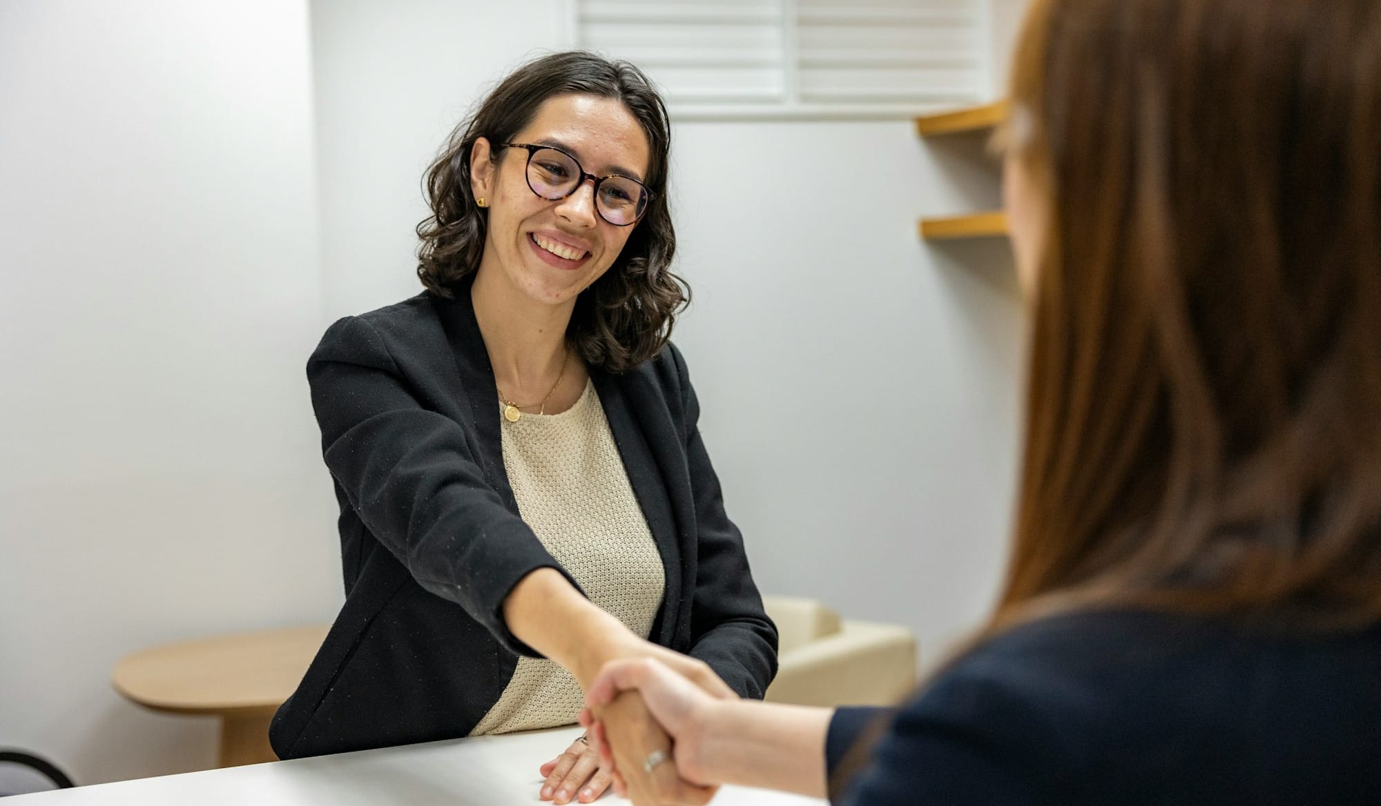 a woman shaking hands with another woman sitting at a table