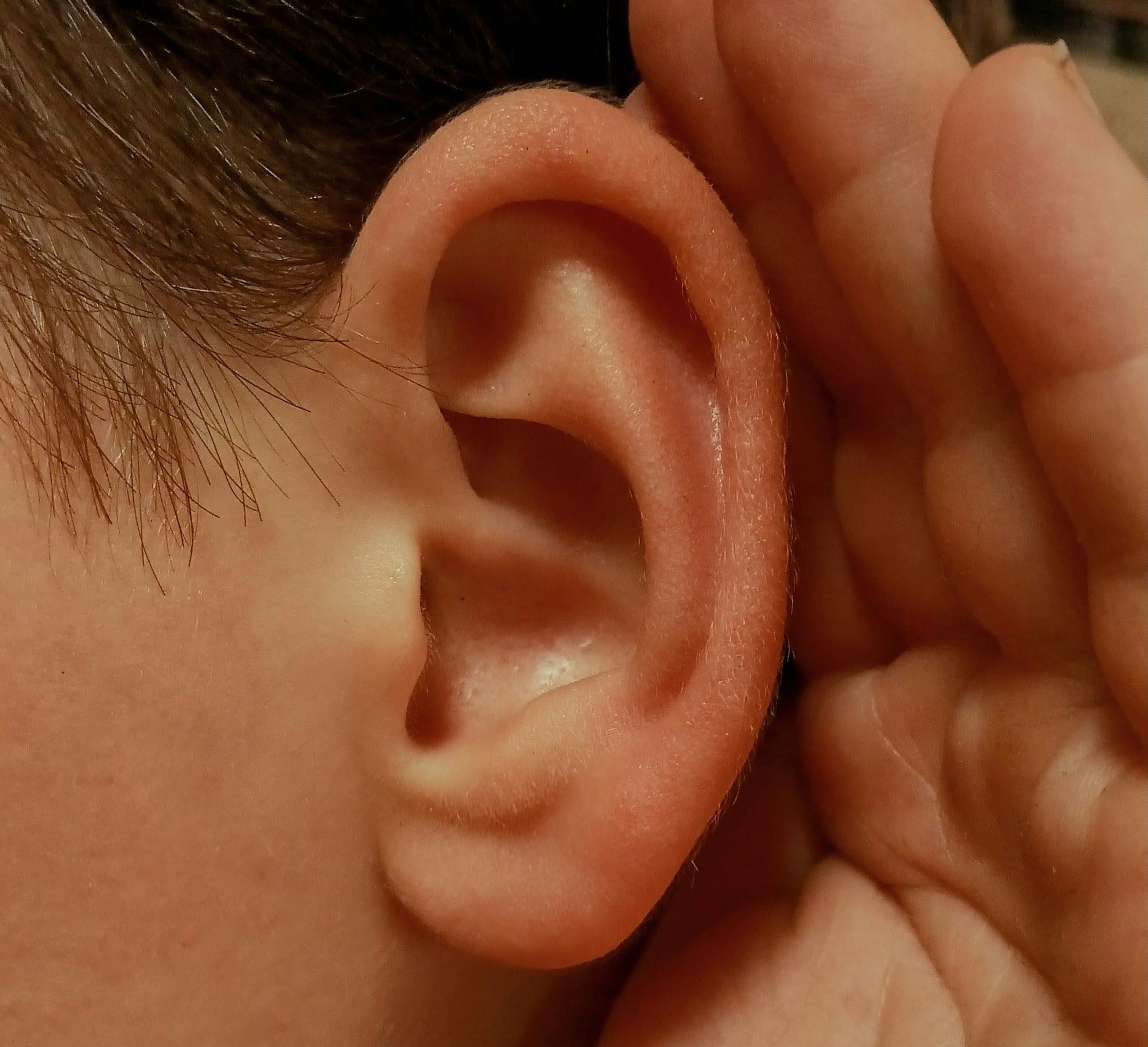 A person cupping their ear to listen closely